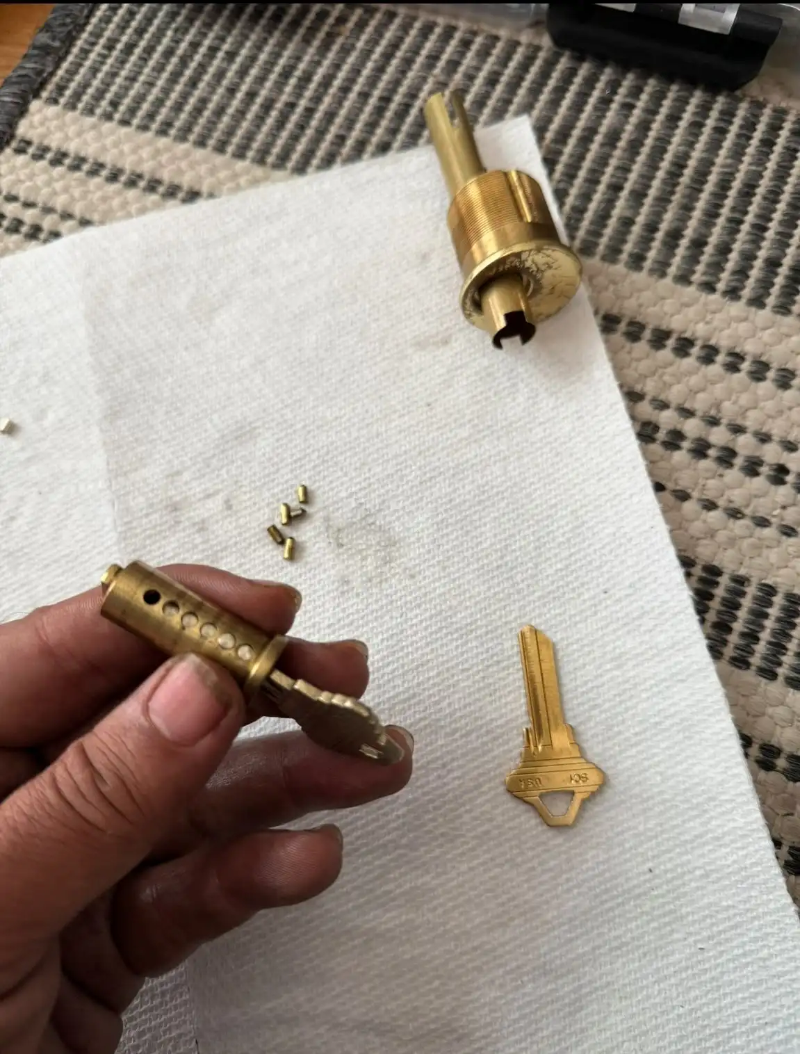 A hand working on disassembling a lock cylinder with pins visible and a key nearby, demonstrating AA Locksmith Near Me LLC's commercial lock rekeying service.