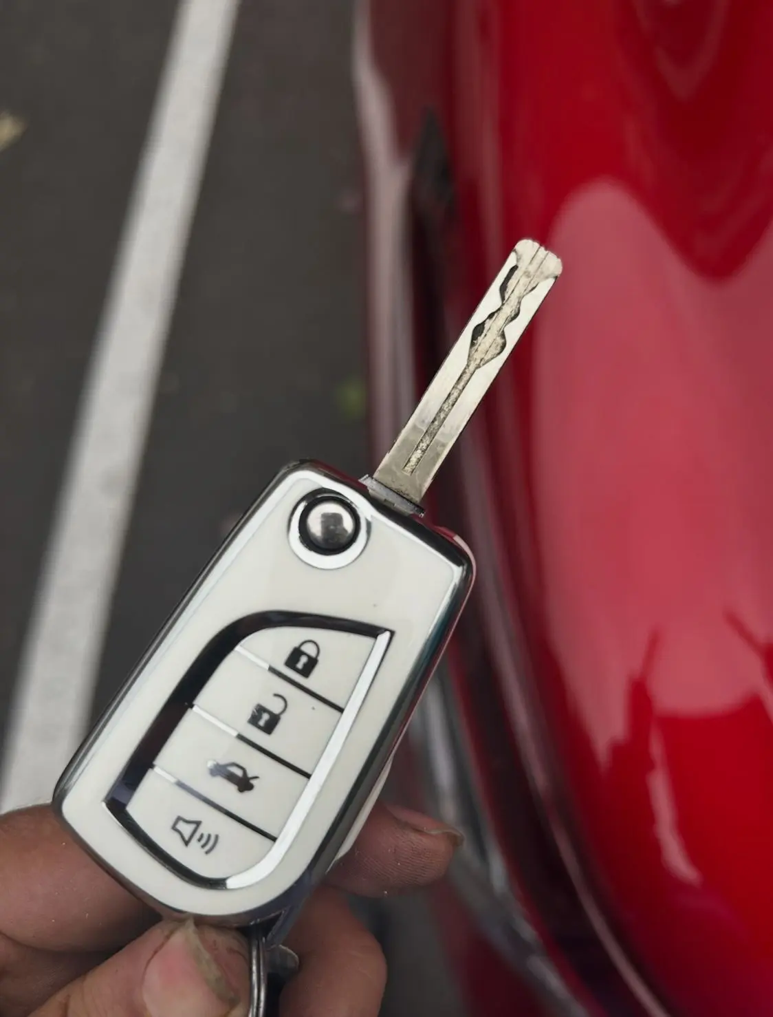 A visibly worn car key held in hand next to a red car, demonstrating the need for AA Locksmith Near Me LLC's ignition repair service.