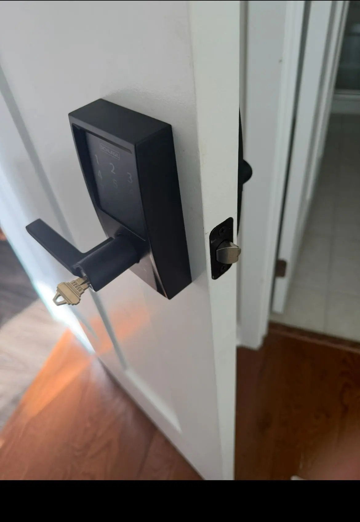 A modern black Schlage smart lock with a key in the handle on a white interior door, representing residential lock replacement services from AA Locksmith Near Me LLC.