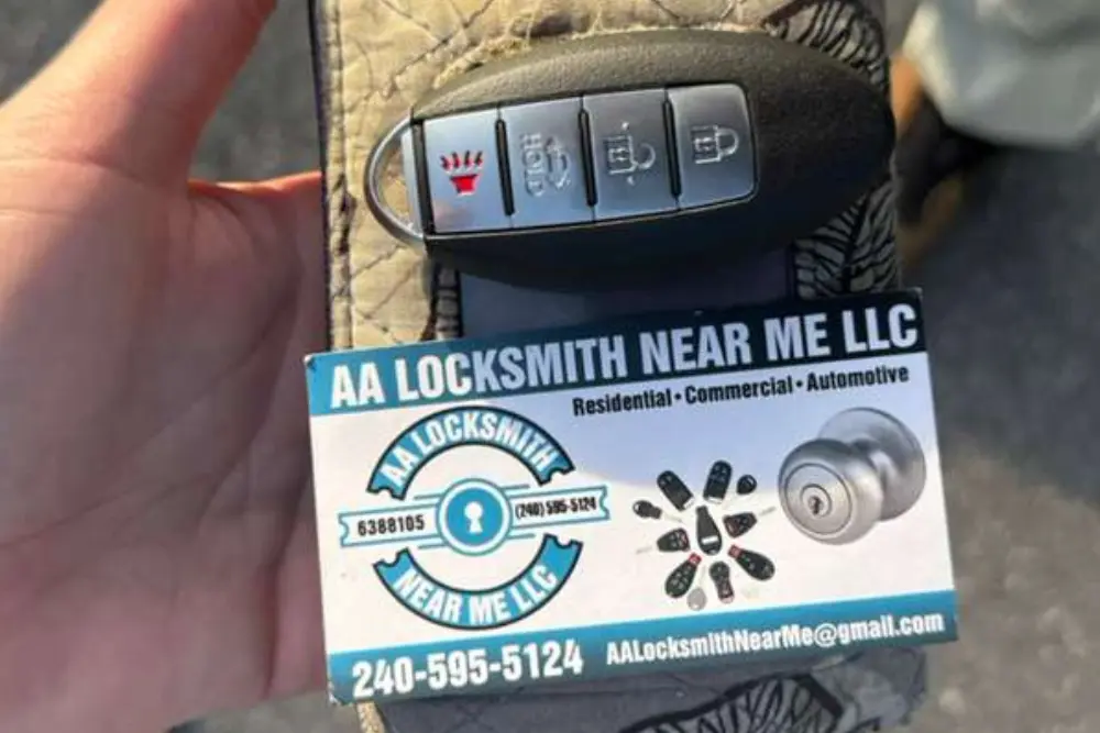 A hand holds an AA Locksmith Near Me LLC business card with a modern 4-button automotive smart key fob resting on top, showcasing a professional locksmith service